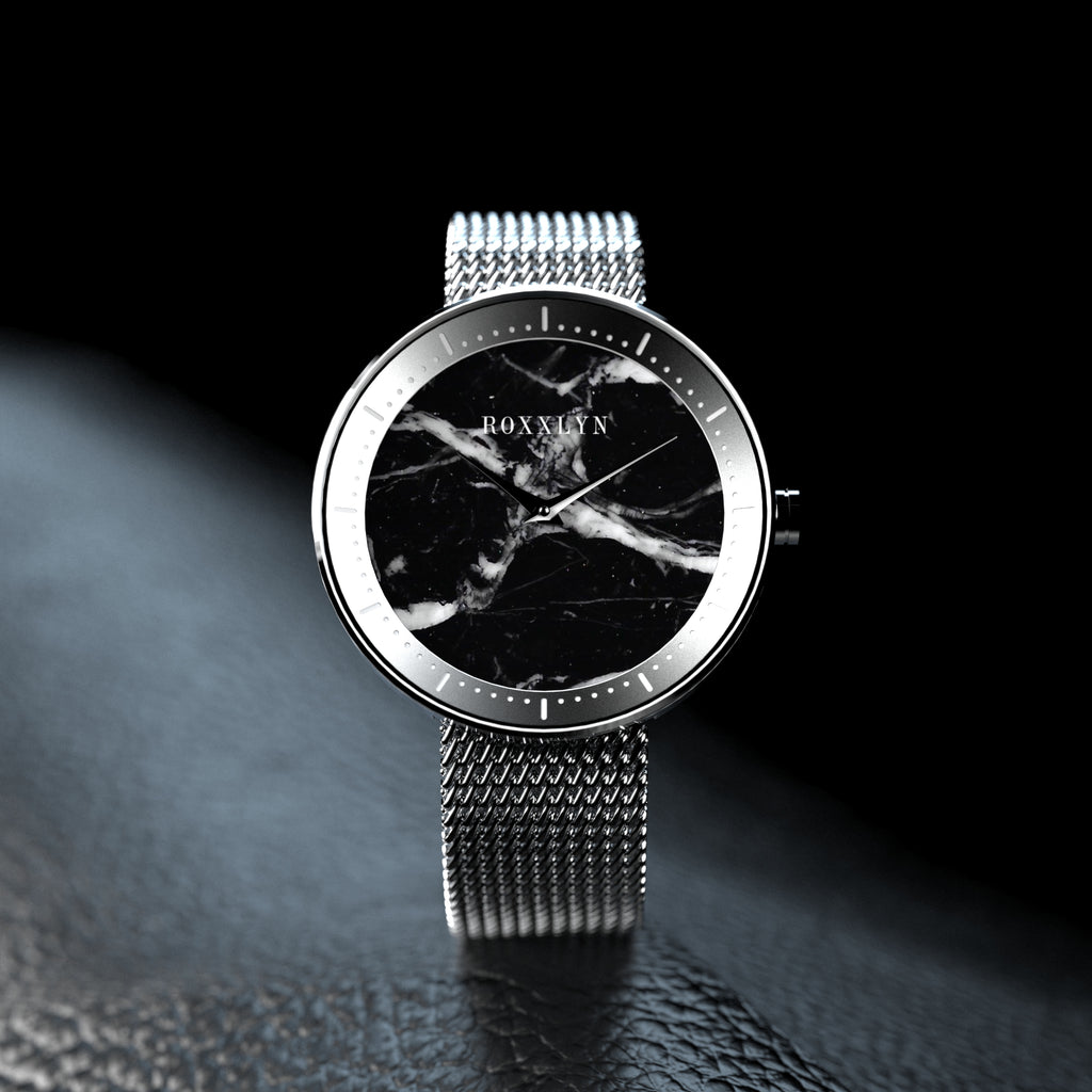 ROXXLYN Marble Watch mit Nero Marquina Zifferblatt und silbernem Milanaise-Armband, auf dunkler Fläche im Streiflicht